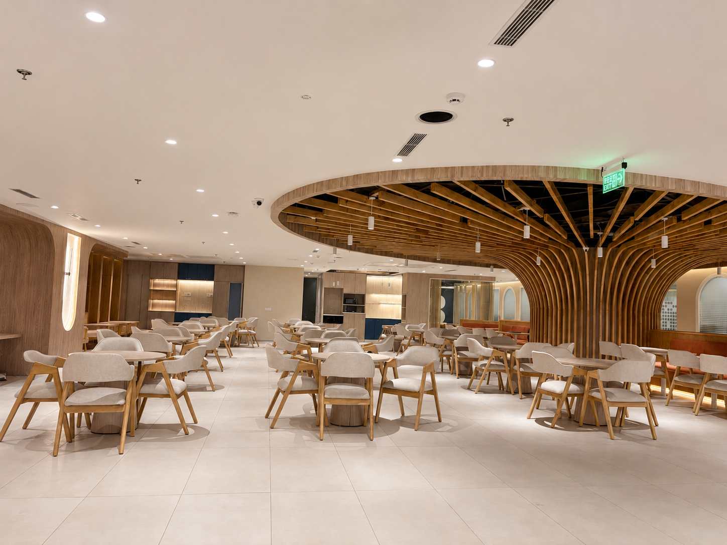 Modern dining area with light wood chairs and tables arranged in rows under a circular wooden ceiling installation and warm lighting.