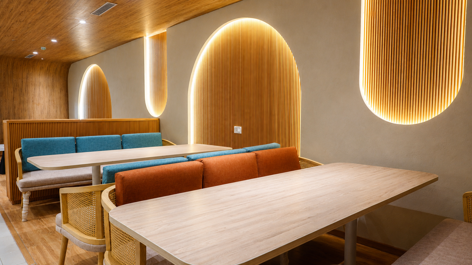 Modern cafe seating area with light wood tables, blue and orange cushions, and backlit circular wall arches.